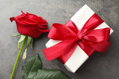 Photo of Gift box with bow and rose on grey table, top view