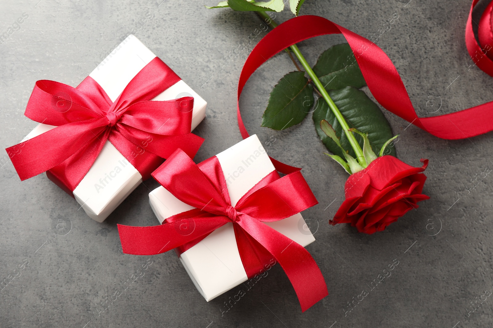 Photo of Gift boxes with bows and rose on grey table, flat lay