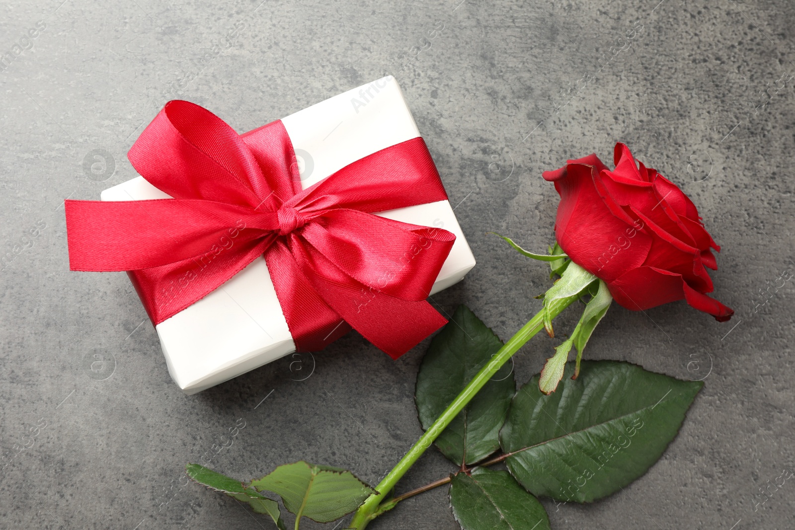 Photo of Gift box with bow and rose on grey table, top view