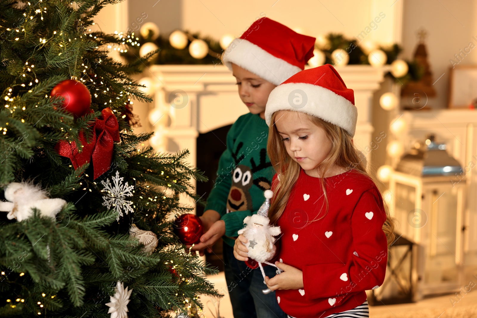 Photo of Little kids in Santa hats decorating Christmas tree at home