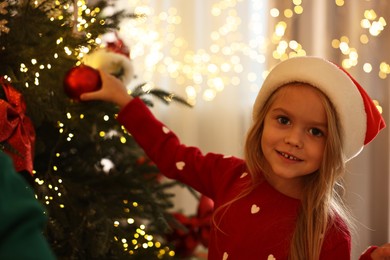 Little girl in Santa hat decorating Christmas tree at home