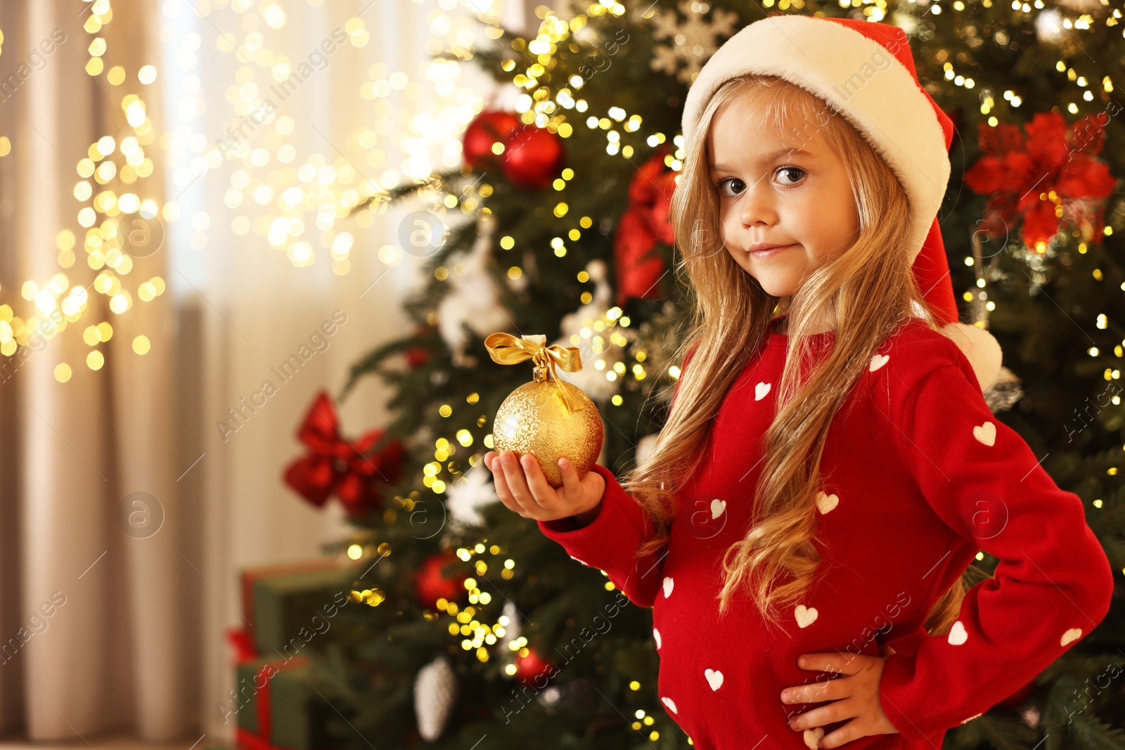 Photo of Little girl in Santa hat with Christmas ball at home, space for text