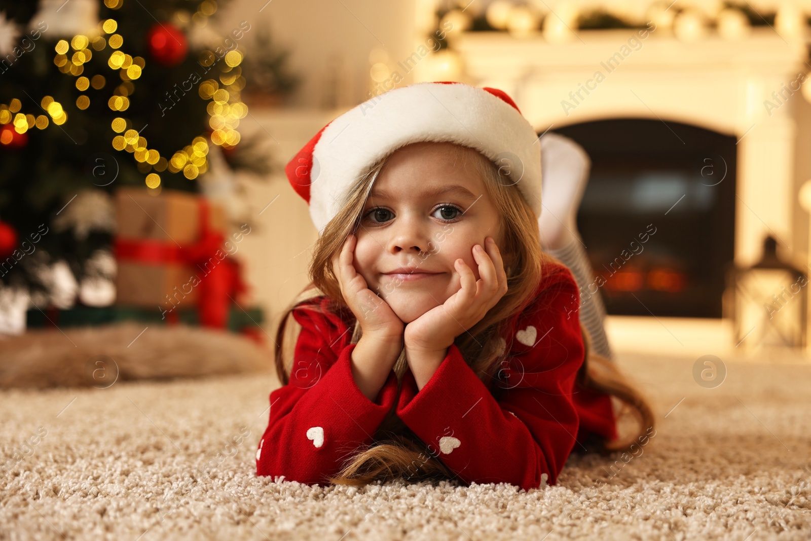 Photo of Little girl in Santa hat on floor at home. Christmas celebration