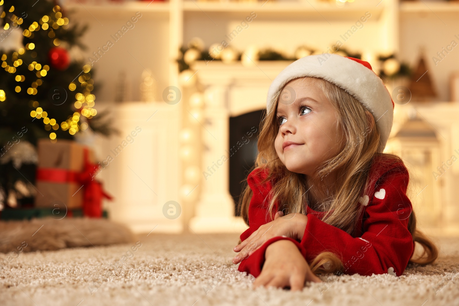 Photo of Little girl in Santa hat on floor at home, space for text. Christmas celebration