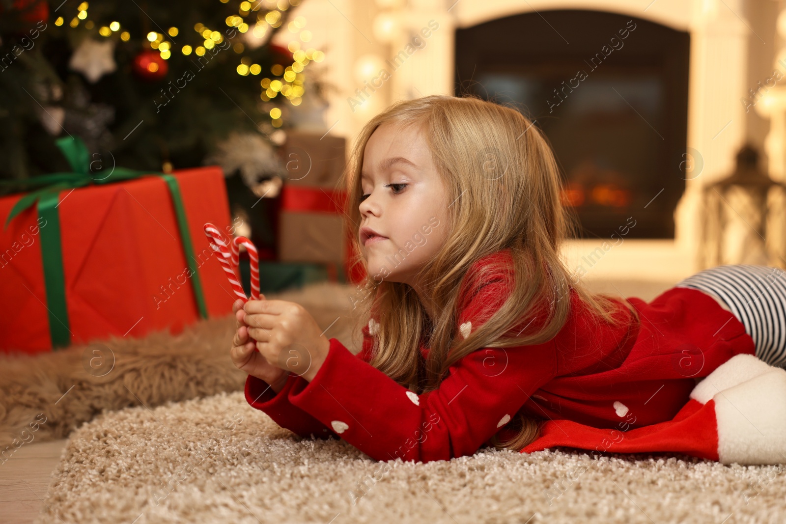 Photo of Little girl with candy canes on floor at home. Christmas celebration