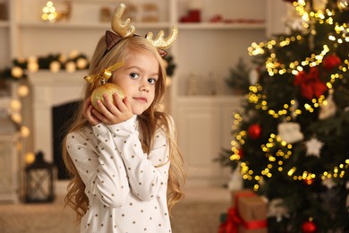 Photo of Little girl with Christmas ornament at home, space for text