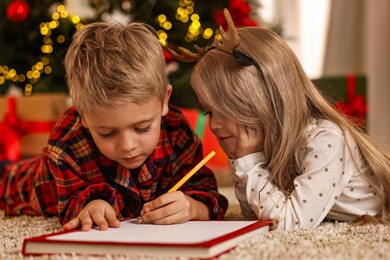 Photo of Little kids writing letter to Santa Claus on floor at home. Christmas celebration