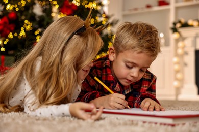 Photo of Little kids writing letter to Santa Claus on floor at home. Christmas celebration