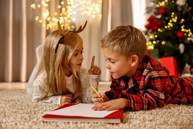 Photo of Little kids writing letter to Santa Claus on floor at home. Christmas celebration