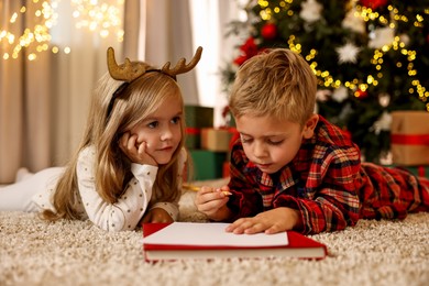 Photo of Little kids writing letter to Santa Claus on floor at home. Christmas celebration