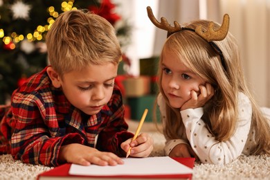 Little kids writing letter to Santa Claus on floor at home. Christmas celebration