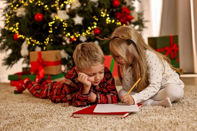 Photo of Little kids writing letter to Santa Claus on floor at home. Christmas celebration