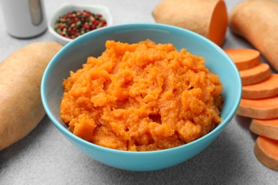 Photo of Tasty mashed sweet potato in bowl and fresh vegetables on gray table, closeup