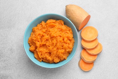 Photo of Tasty mashed sweet potato in bowl and cut vegetable on gray table, flat lay