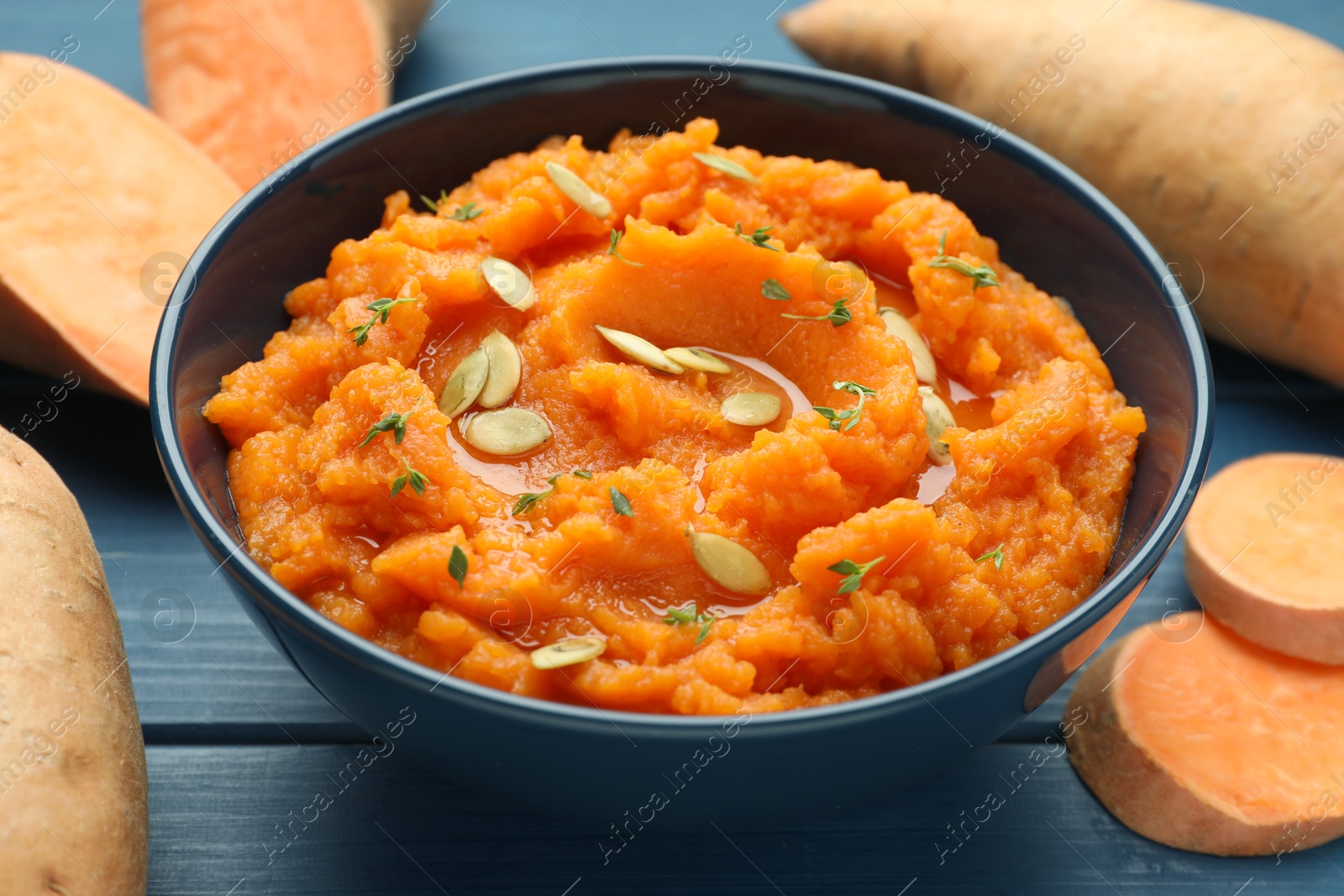 Tasty mashed sweet potato with pumpkin seeds in bowl and fresh vegetables on blue wooden table, closeup Photo of Tasty mashed sweet potato with pumpkin seeds in bowl and fresh vegetables on blue wooden table, closeup