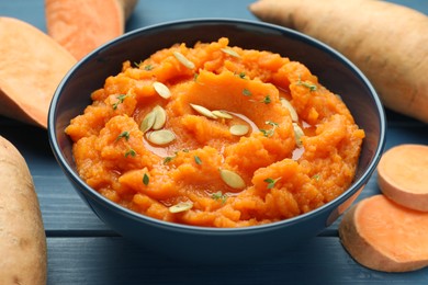 Photo of Tasty mashed sweet potato with pumpkin seeds in bowl and fresh vegetables on blue wooden table, closeup