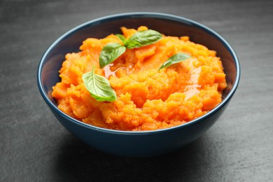 Photo of Tasty mashed sweet potato with basil in bowl on dark gray textured table, closeup