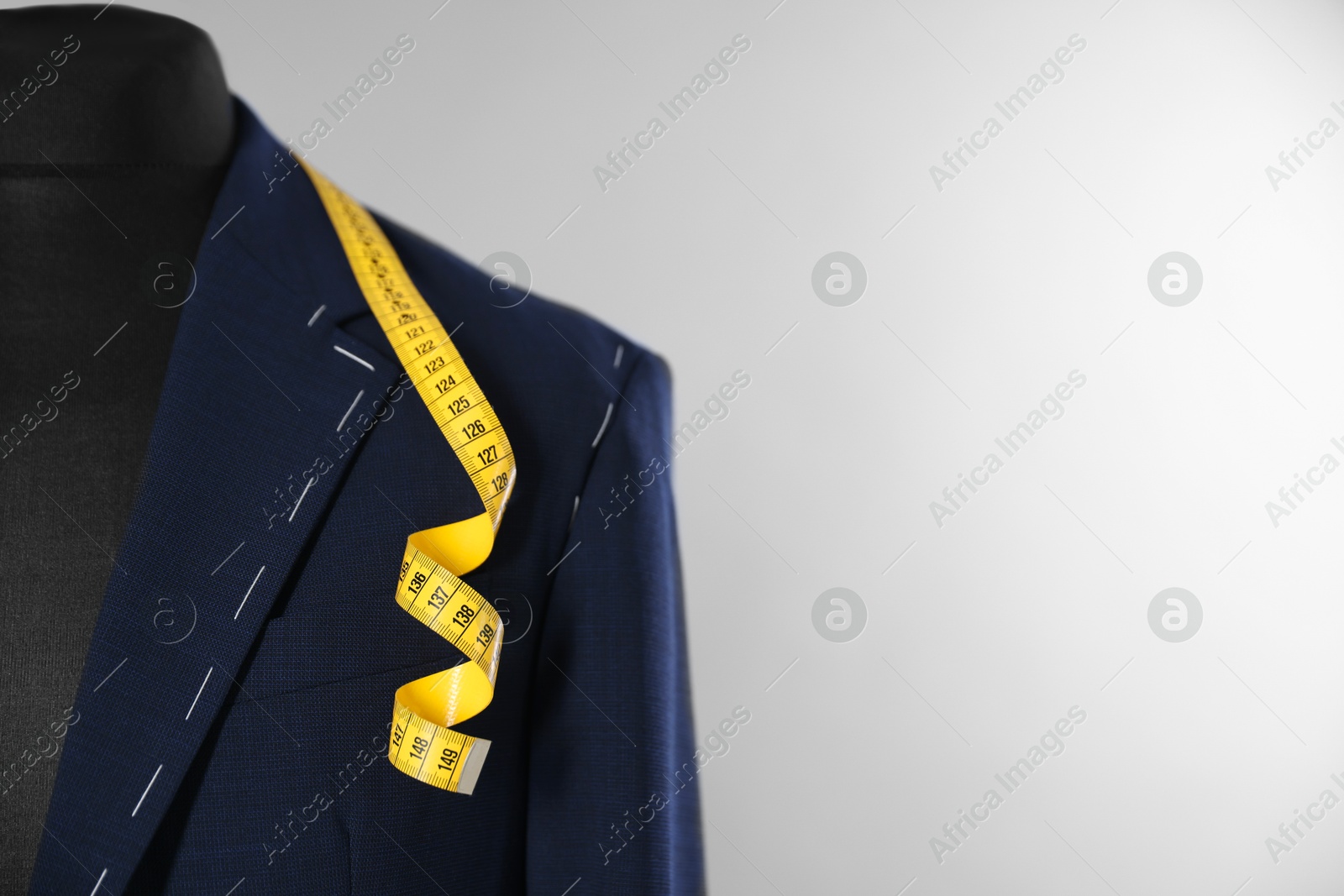 Photo of Semi-ready jacket and measuring tape on mannequin against gray background, closeup. Space for text