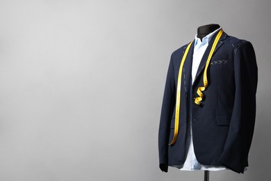 Photo of Semi-ready jacket, shirt and measuring tape on mannequin against gray background, space for text