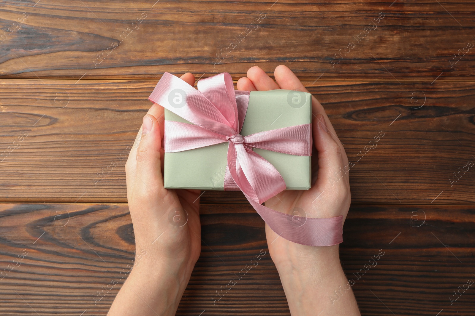 Photo of Woman holding gift box with pink bow on wooden table, top view