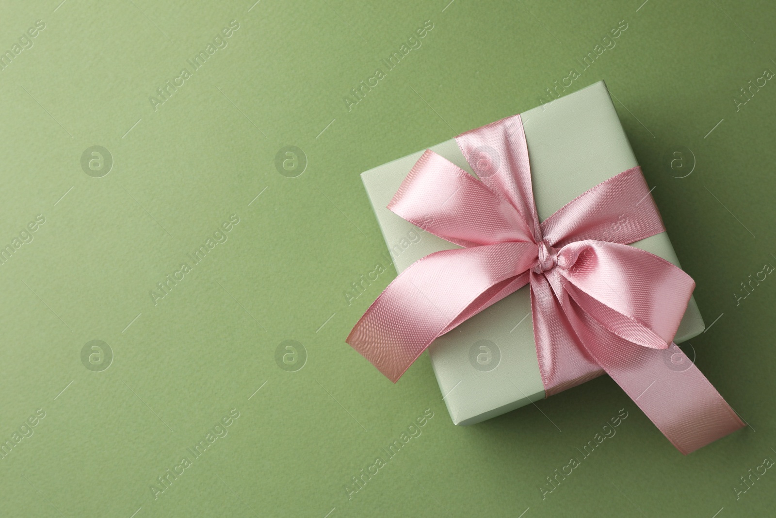 Photo of Gift box with pink bow on green background, top view. Space for text