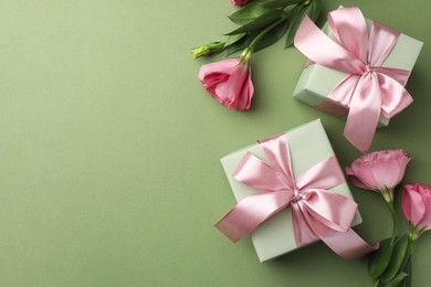 Gift boxes with pink bows and beautiful flowers on green background, flat lay. Space for text