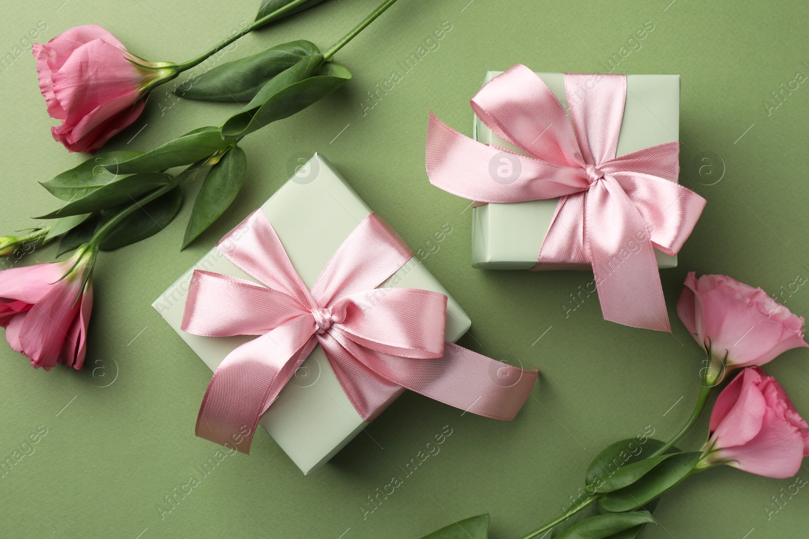 Photo of Gift boxes with pink bows and beautiful flowers on green background, flat lay