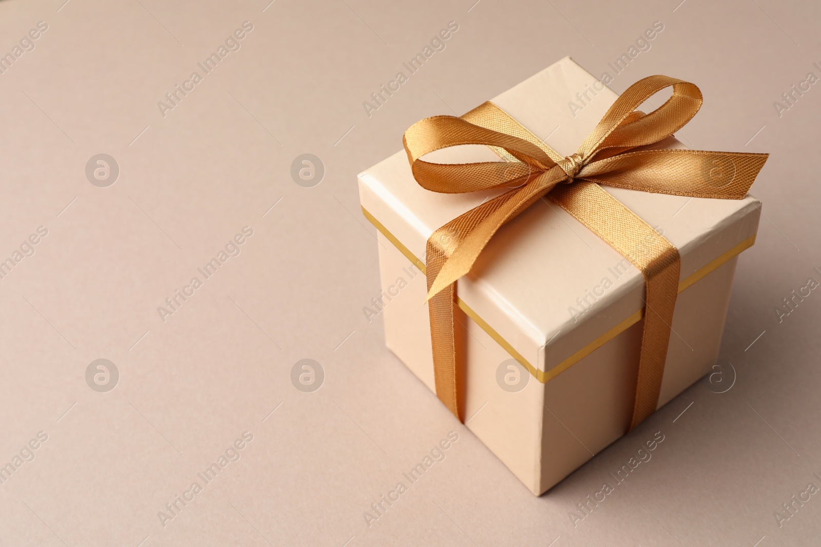 Photo of Gift box with golden bow on beige background, closeup. Space for text