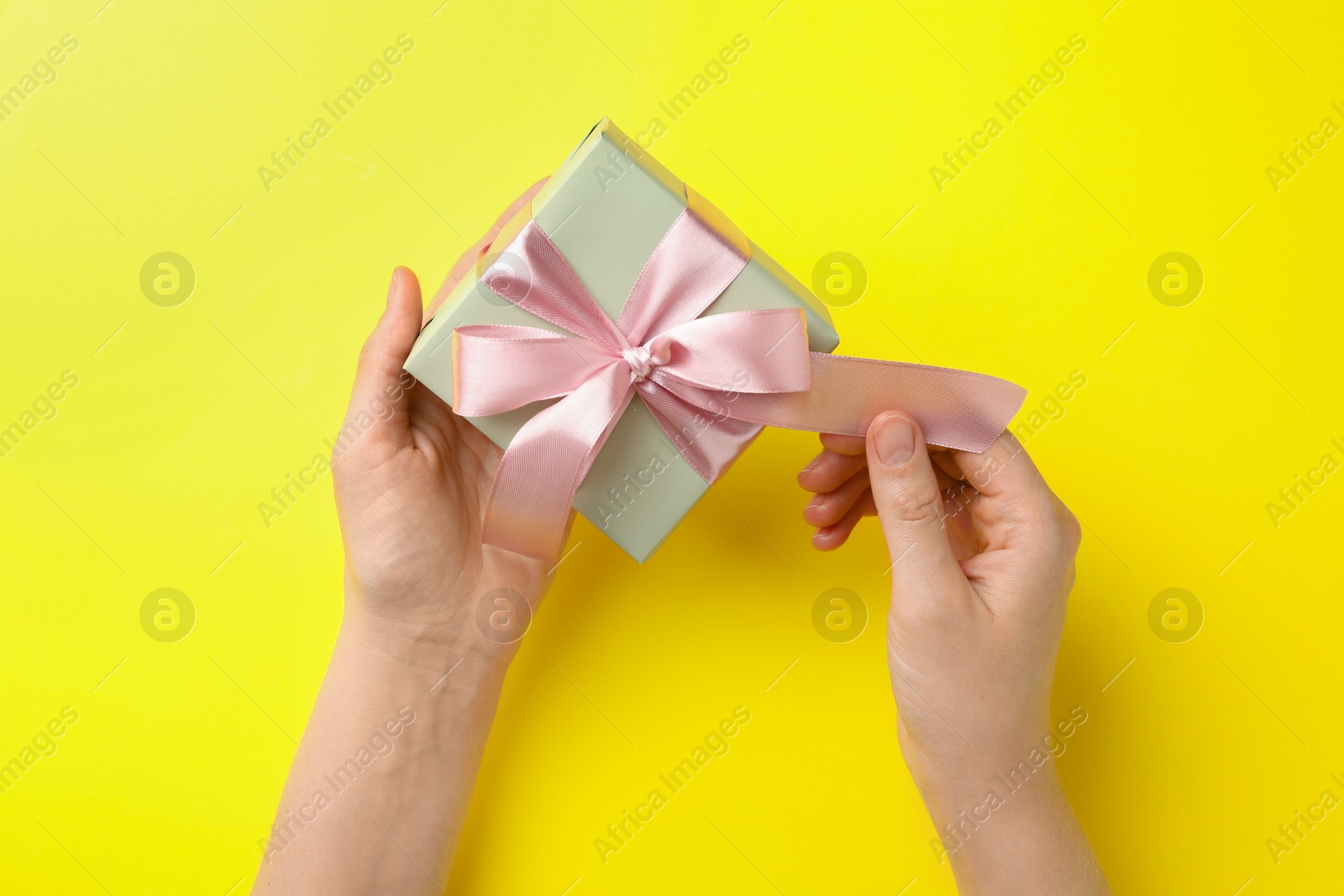 Photo of Woman holding gift box with pink bow on yellow background, top view