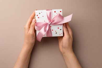 Woman holding gift box with pink bow on beige background, top view