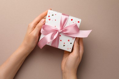 Photo of Woman holding gift box with pink bow on beige background, top view