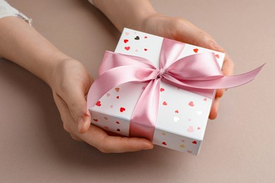 Photo of Woman holding gift box with pink bow on beige background, closeup