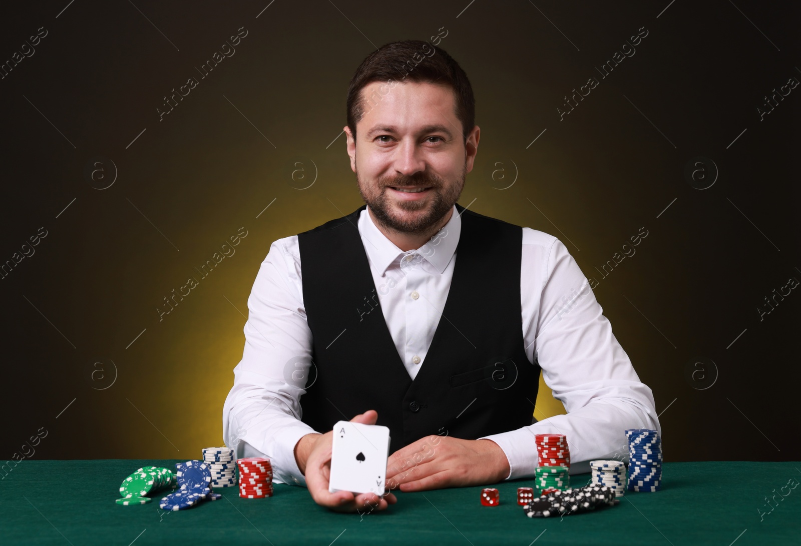 Photo of Professional croupier with playing cards at gambling table against dark yellow background