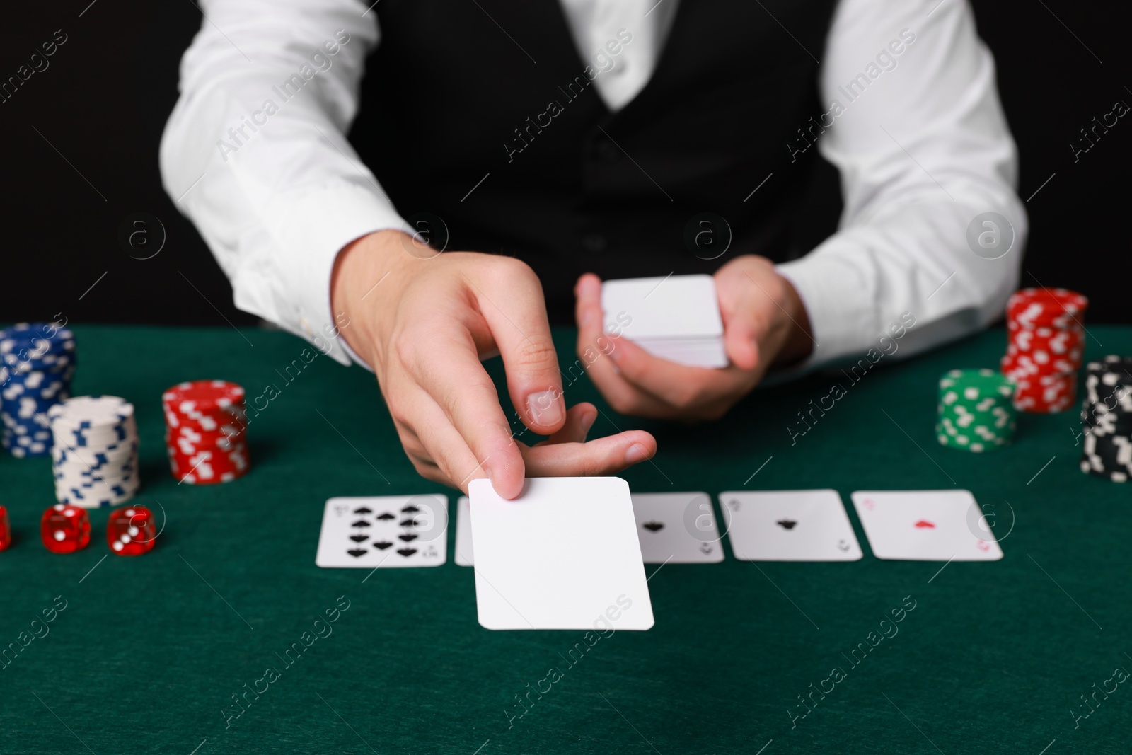 Photo of Professional croupier with playing cards at gambling table, closeup