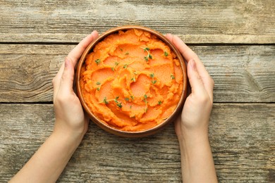 Photo of Woman with bowl of tasty mashed sweet potato at wooden table, top view