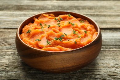 Photo of Tasty mashed sweet potato with thyme in bowl on wooden table, closeup