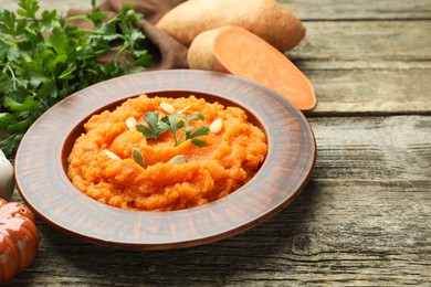 Photo of Tasty mashed sweet potato with pumpkin seeds in bowl, fresh vegetables and parsley on wooden table, closeup