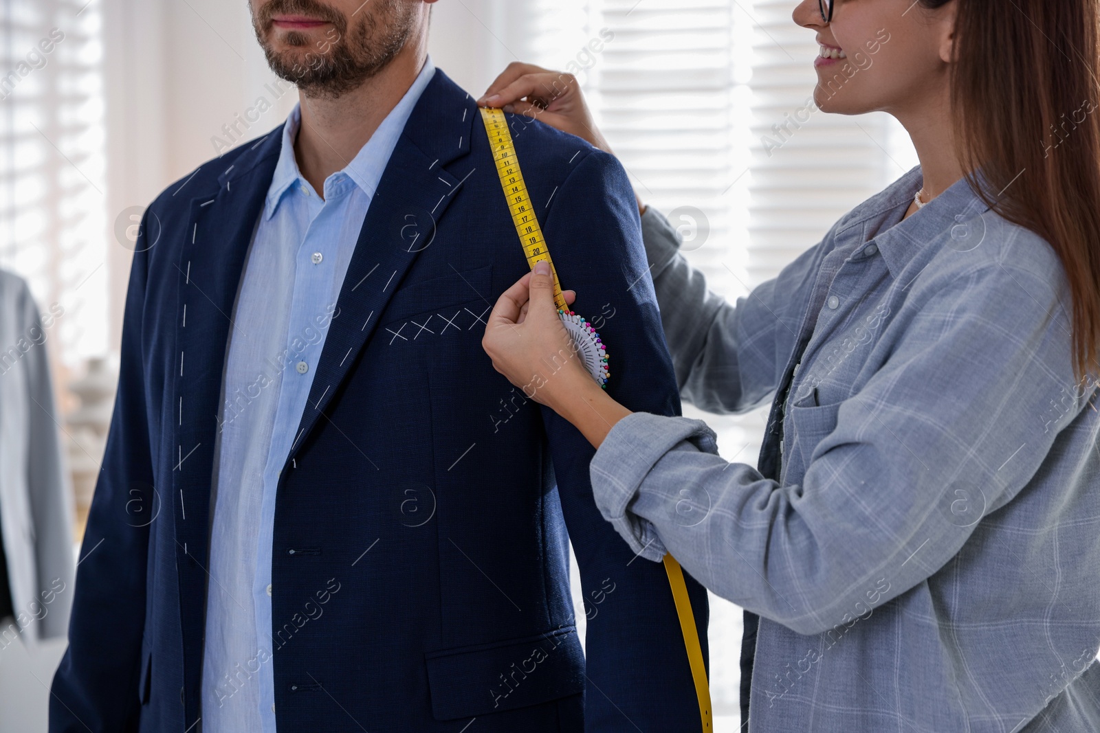 Photo of Tailor measuring jacket on man during fitting in atelier, closeup