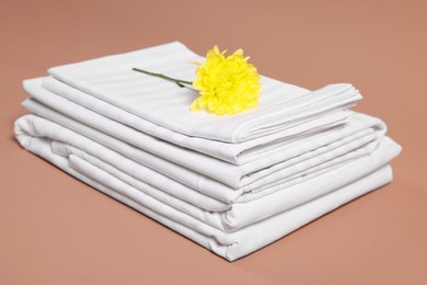 Photo of Stack of clean bed linens and beautiful flower on beige background, closeup