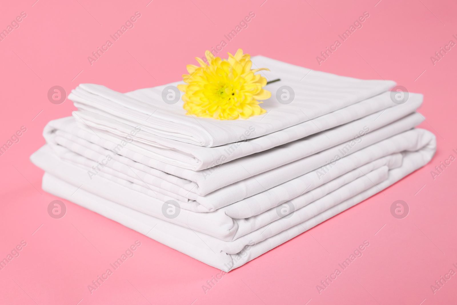 Photo of Stack of clean bed linens and beautiful flower on pink background, closeup