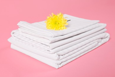 Photo of Stack of clean bed linens and beautiful flower on pink background, closeup