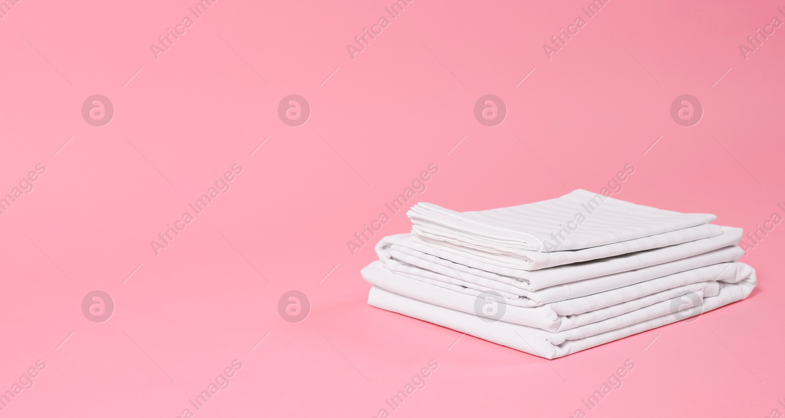 Photo of Stack of clean bed linens on pink background, space for text