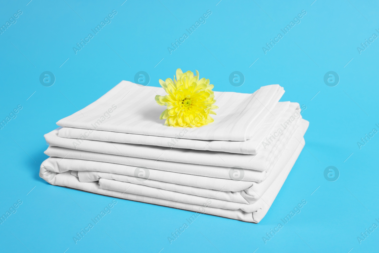 Photo of Stack of clean bed linens and beautiful flower on light blue background