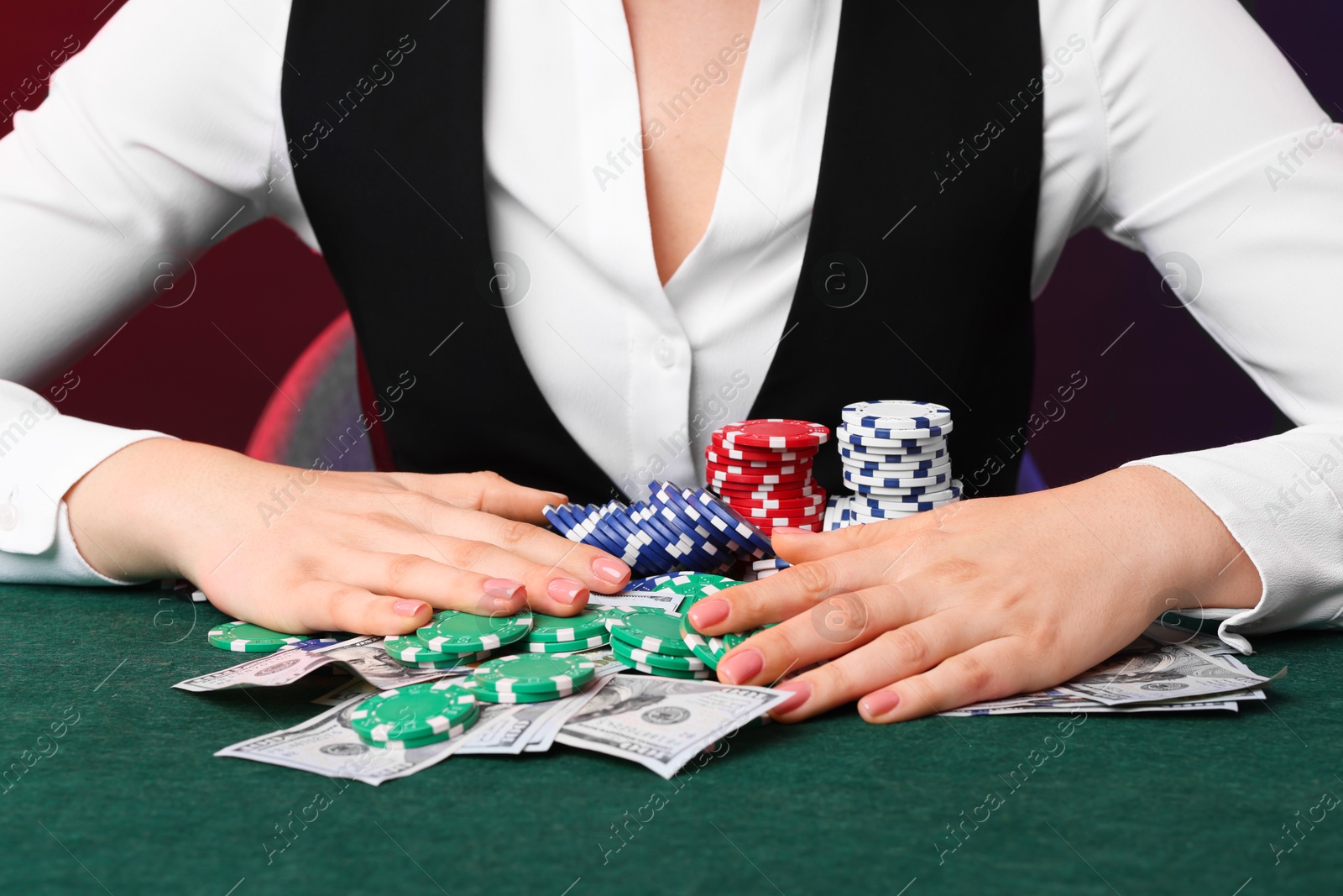 Photo of Professional croupier with casino chips and playing cards at gambling table on color background, closeup