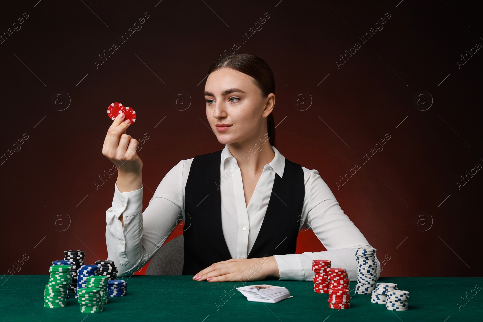 Photo of Professional croupier with casino chips and playing cards at gambling table on color background