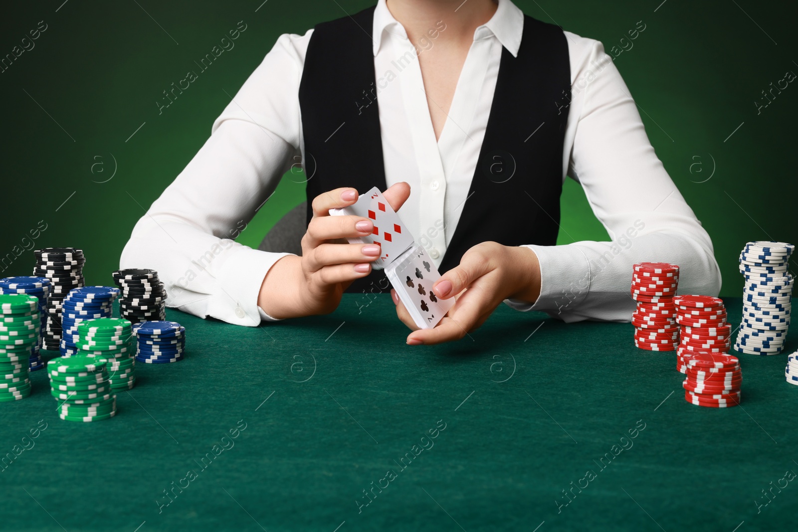 Photo of Professional croupier with casino chips and playing cards at gambling table on color background, closeup