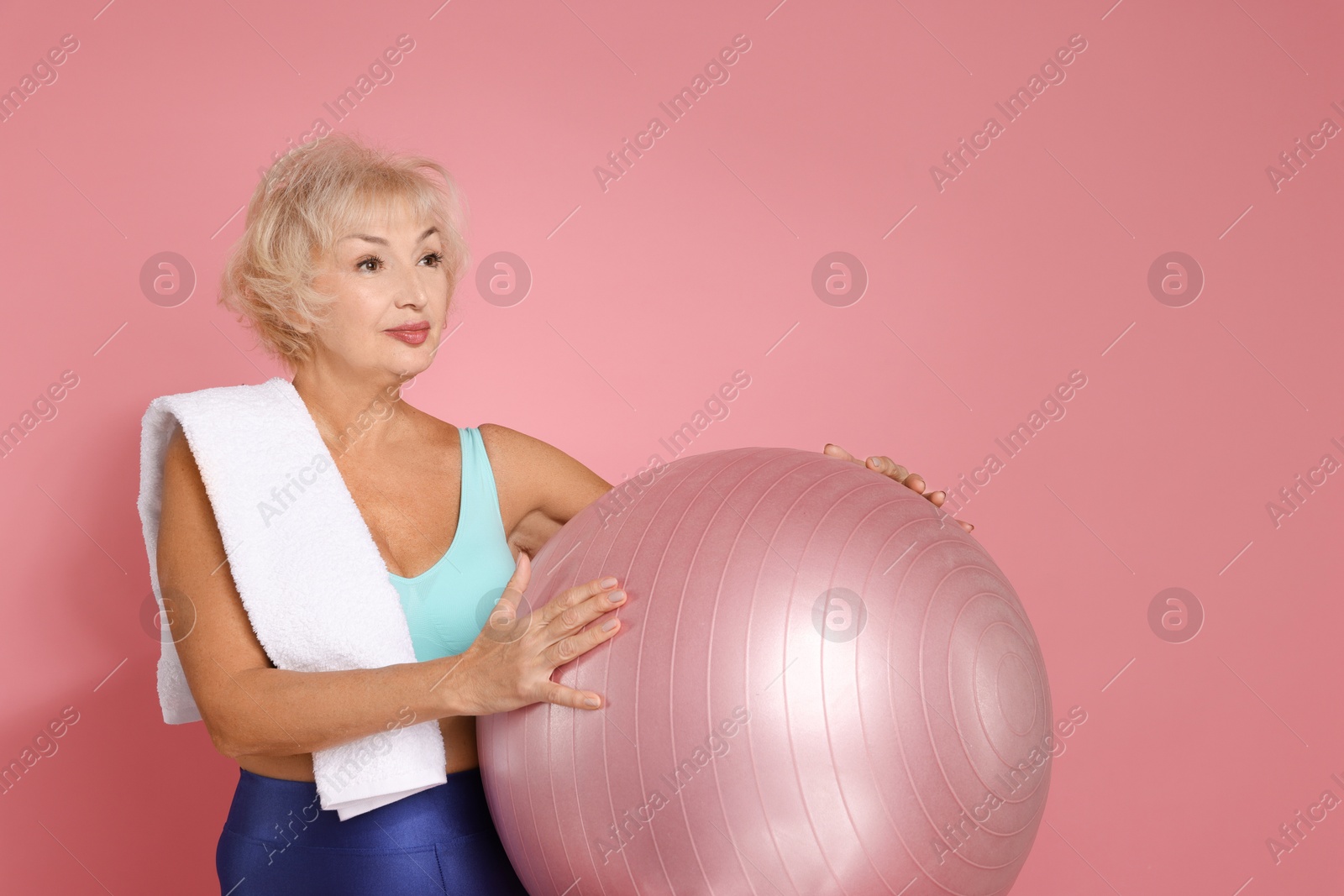 Photo of Senior woman with towel and fitness ball on pink background. Space for text