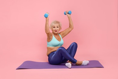 Photo of Senior woman exercising with fitness mat and dumbbells on pink background