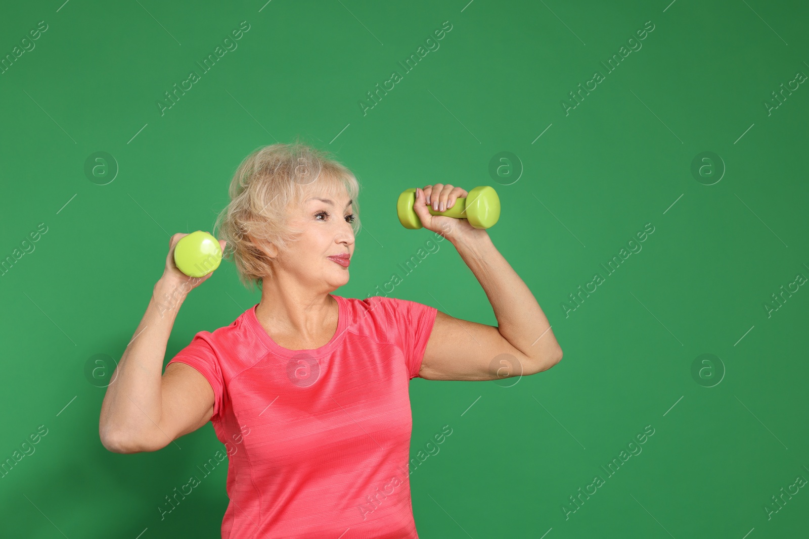 Photo of Senior woman exercising with dumbbells on green background, space for text