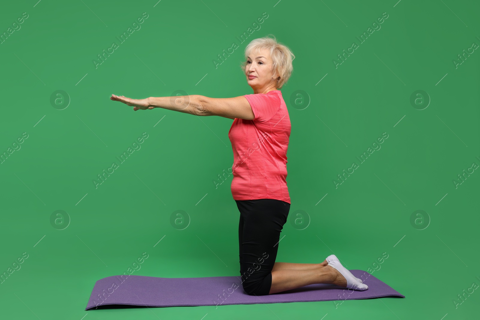 Photo of Senior woman exercising with fitness mat on green background